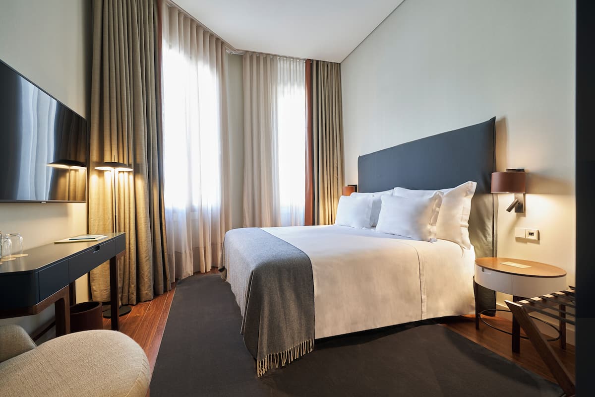 Ett hotellrum med en säng, ett skrivbord, en stol, en lampa och gardiner.