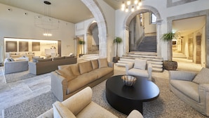 A spacious living area with a large sectional sofa, a round coffee table, and a fireplace. There are multiple seating options including armchairs and a couch. The room features a high ceiling with exposed beams and a staircase leading to an upper level. - PortoBay Flores (Porto)