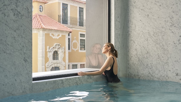 Une personne se détend dans un bain à remous, avec vue sur un bâtiment dont le toit est recouvert de tuiles rouges.