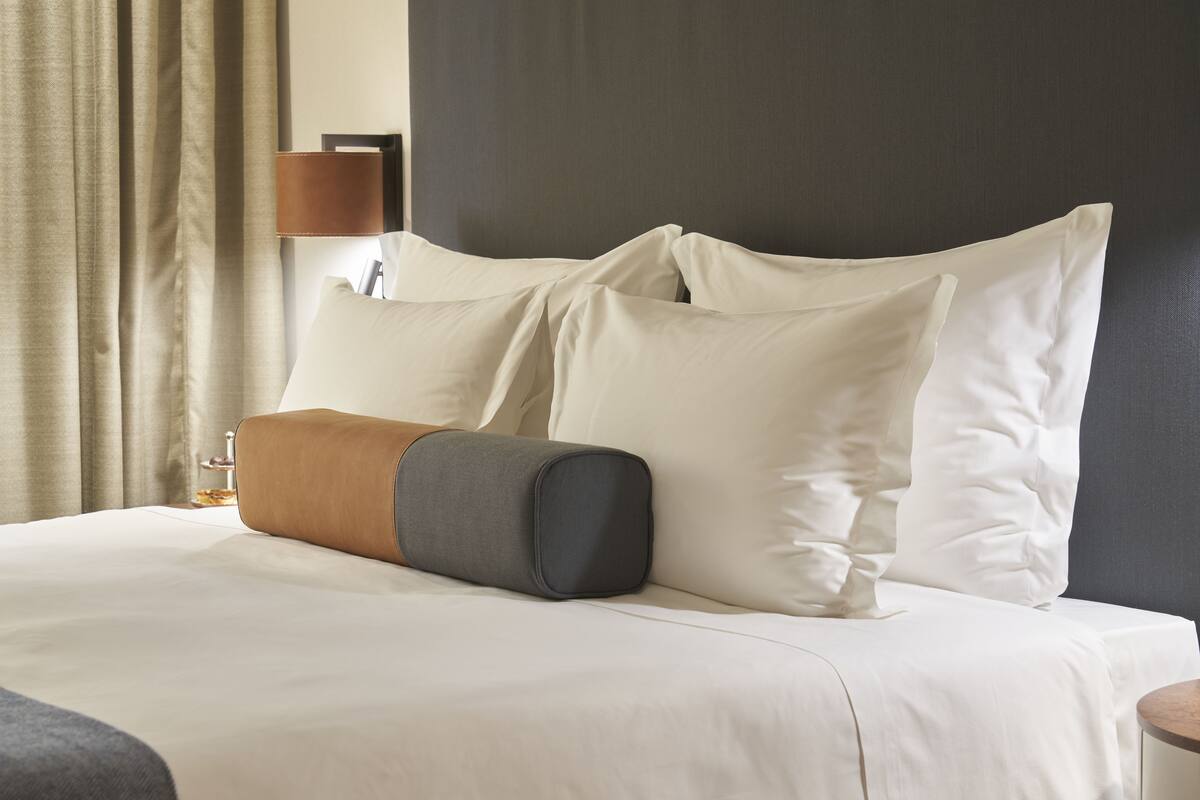 A neatly made bed with multiple pillows and a lamp on a bedside table.