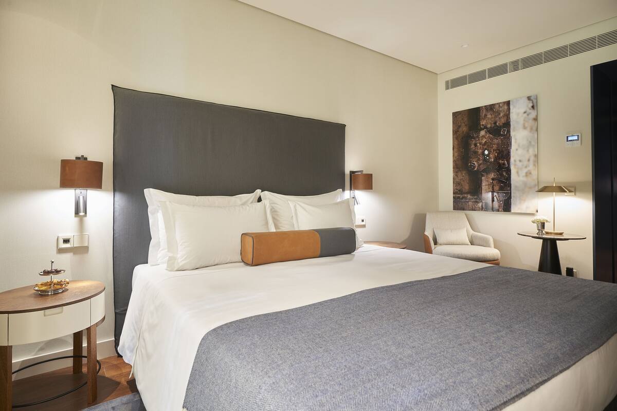 A hotel room with a large bed, two bedside tables, a chair, and a wall-mounted artwork.