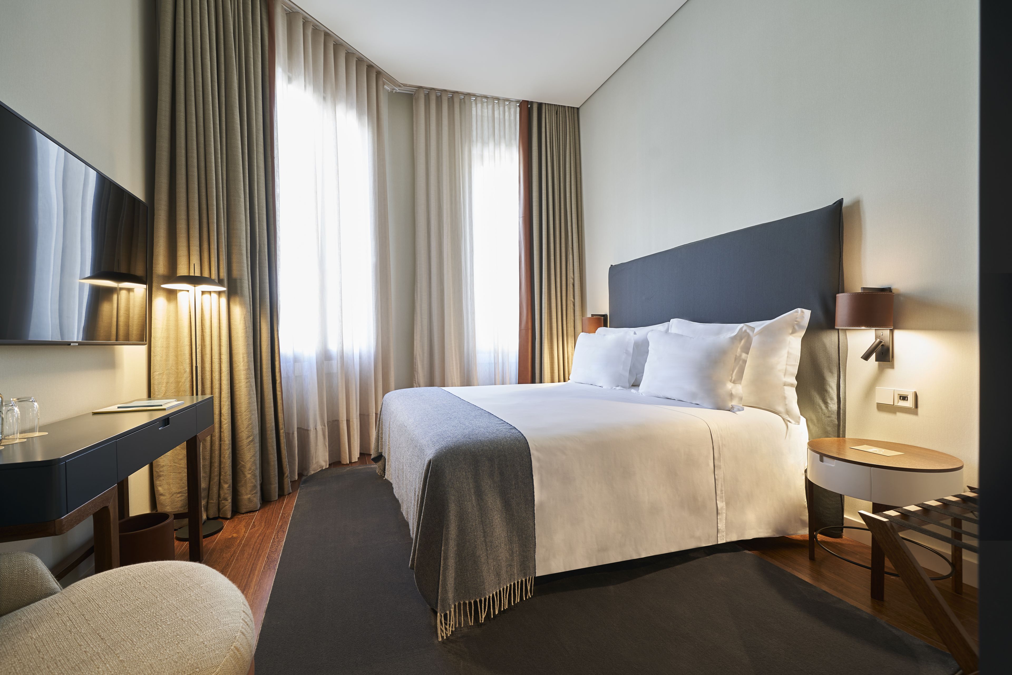 Una habitación de hotel con una cama grande, un escritorio, una silla, un televisor y una lámpara.