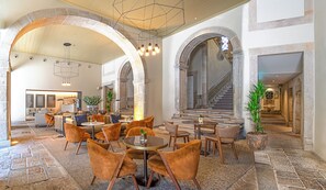 A spacious lobby with high ceilings, arched stone columns, and a staircase leading to an upper level. - PortoBay Flores (Porto)
