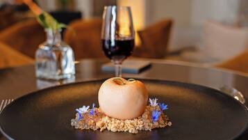 Un postre en un plato con una copa de vino tinto y un jarrón con flores.
