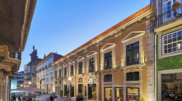 A historic building with a covered outdoor seating area and shops on the ground floor.
