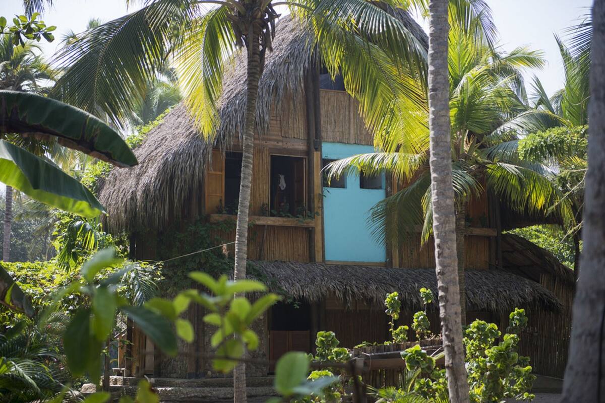 A traditional thatched-roof building with multiple balconies, surrounded by lush tropical vegetation.