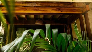 Un balcon en bois orné d’une balustrade en fer forgé, entouré d’un luxuriant feuillage verdoyant.