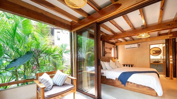 Une chambre avec un lit, une chaise et une vue sur une végétation luxuriante.