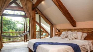 Une chambre avec un grand lit, des poutres en bois, un hamac et une vue sur la verdure.
