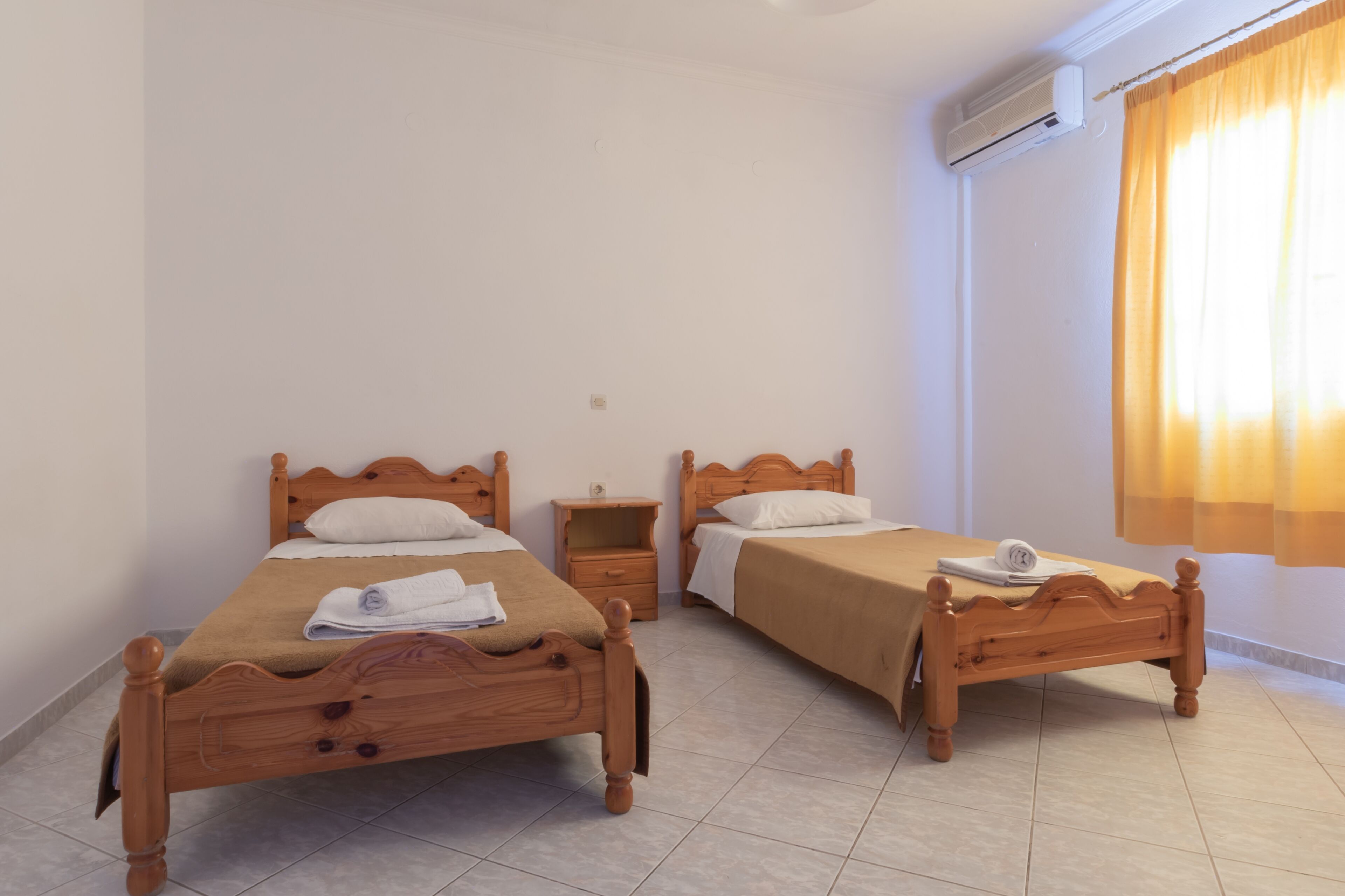 Une chambre avec deux lits en bois, une table de chevet et un climatiseur fixé au mur.