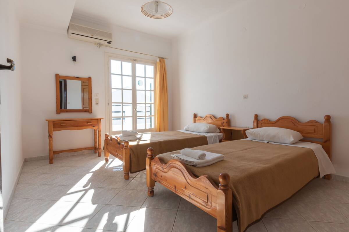 Habitación de hotel con dos camas de madera, un escritorio pequeño de madera, un espejo y una ventana con cortinas.