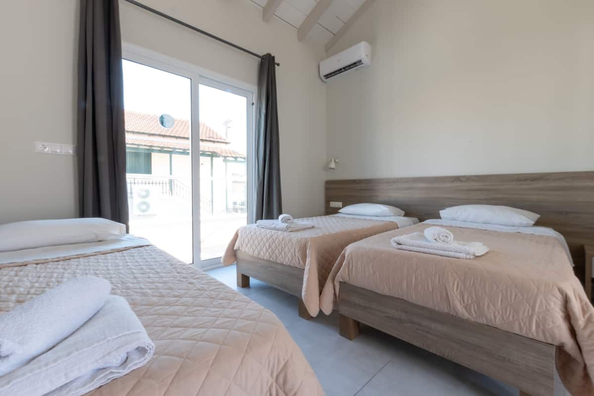Habitación de hotel con dos camas, cada una con cabecero de madera, y un amplio ventanal corredero que da a un espacio exterior.