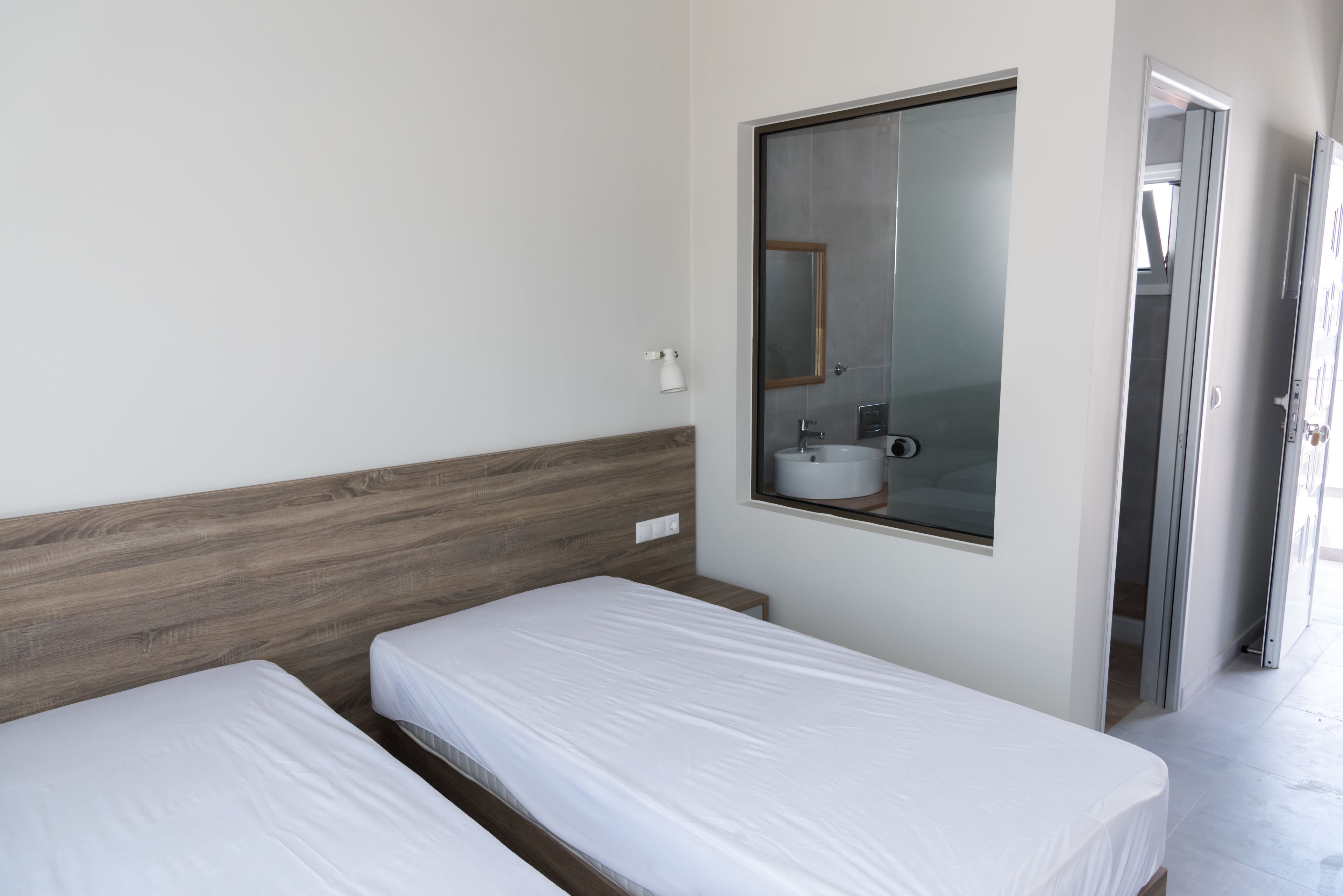 A hotel room with two single beds, a small bedside table, a mirror, and a window.