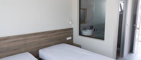A hotel room with two single beds, a small bedside table, a mirror, and a window.