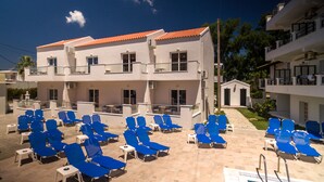A hotel with a pool area featuring blue lounge chairs and a tiled deck. - The Barn by CorfuEscapes (Corfu)