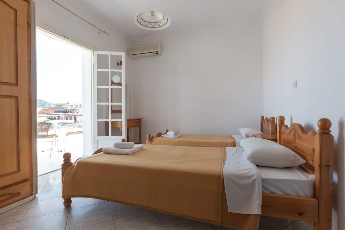 Habitación con dos camas de madera, un equipo de aire acondicionado blanco y vista al exterior por una puerta abierta.