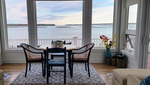 A dining area with a table and chairs, a vase with flowers, and a view of the water through large windows. - The Dream chalet  (Cocagne)