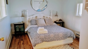 A neatly made bed with patterned bedding and a bedside lamp, a small bedside table with a lamp, and a wall-mounted mirror. - The Dream chalet  (Cocagne)