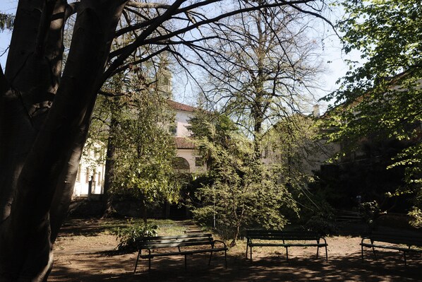 Un parc avec des bancs et des arbres, et en arrière-plan, un bâtiment avec un toit en tuiles.