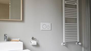 Une salle de bain moderne avec un meuble-lavabo blanc, des toilettes, un bidet, un porte-serviettes et un miroir.