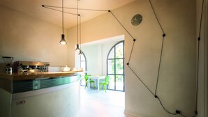 A modern kitchen with a built-in espresso machine, a dining area with a table and chairs, and a large window providing natural light. - Oasi di Cavoretto 97 - Casa per Ferie (Turin)