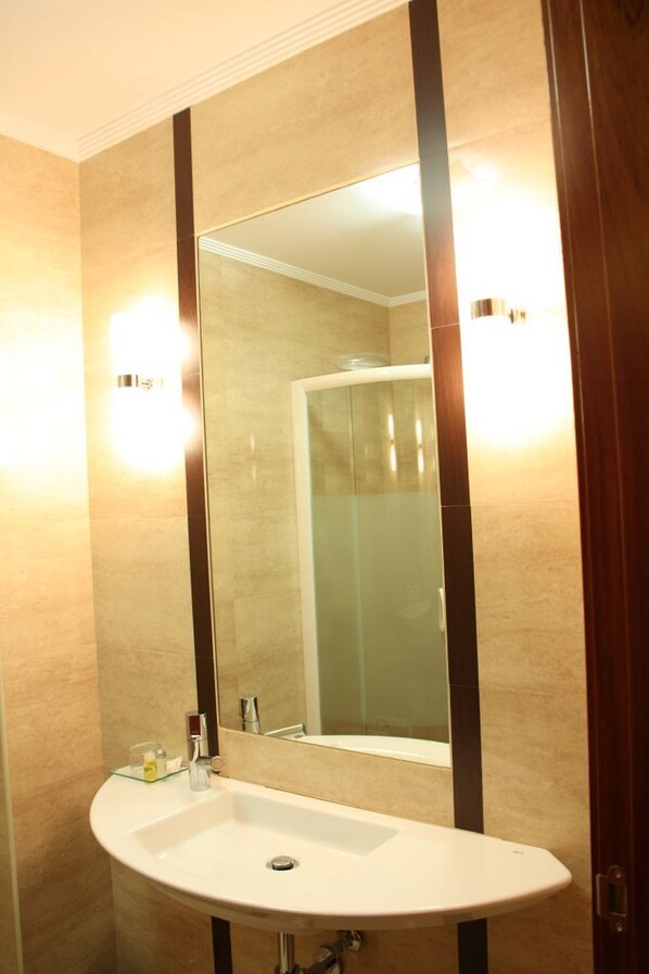 Un baño con un lavamanos blanco, un espejo grande y una cabina de ducha con paredes de vidrio.