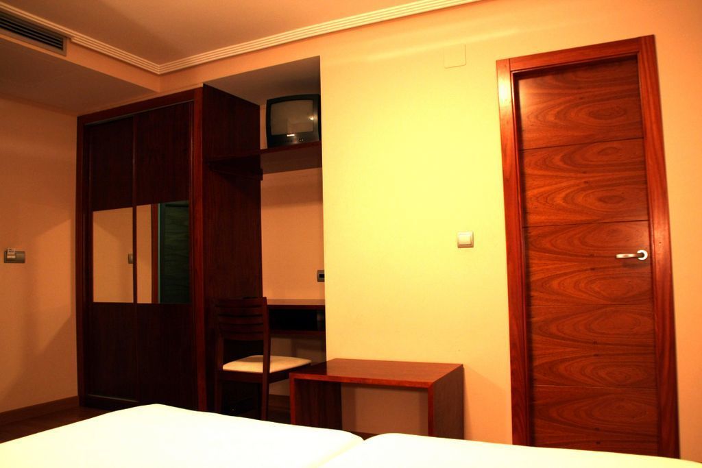 Habitación de hotel con cama, armario de madera, una mesita y televisor en un estante.
