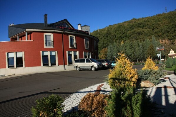 A red brick building with a curved facade, a white car parked in front, and a forested hillside in the background. - Tremazal Hotel (Guardo)