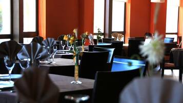 Un restaurante con mesas dispuestas para comer, adornado con jarrones de flores y una cálida pared color naranja.