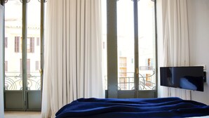 A hotel room with a bed, a TV, and a balcony with curtains.