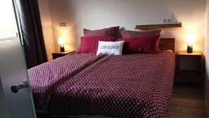 Una cama bien hecha con una colcha y almohadas estampadas, dos lámparas de noche, un estante con un objeto pequeño y una puerta con manija.