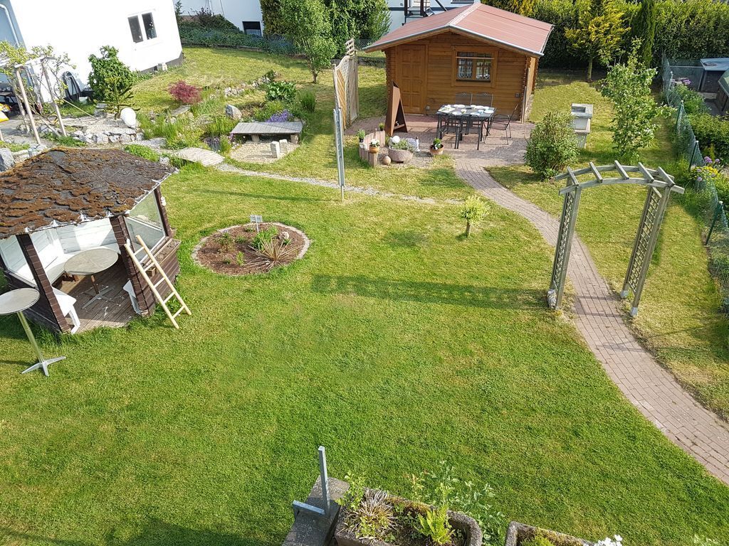 A well-maintained garden with a wooden cabin, a small patio area, and a paved walkway.
