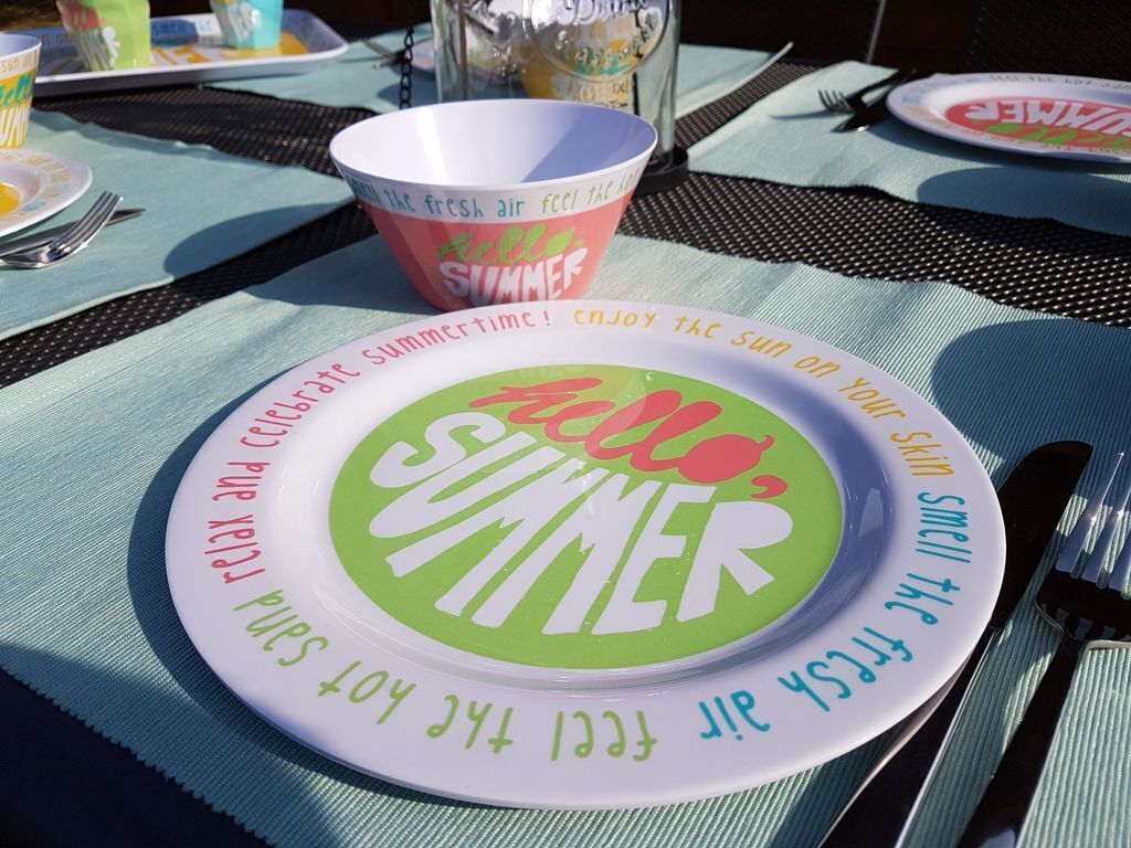 Eine gedeckte Tafel mit einem Teller, auf dem 'Hello Summer' steht, und einer Schüssel mit der Aufschrift 'Fresh Air Feel the Sun'.