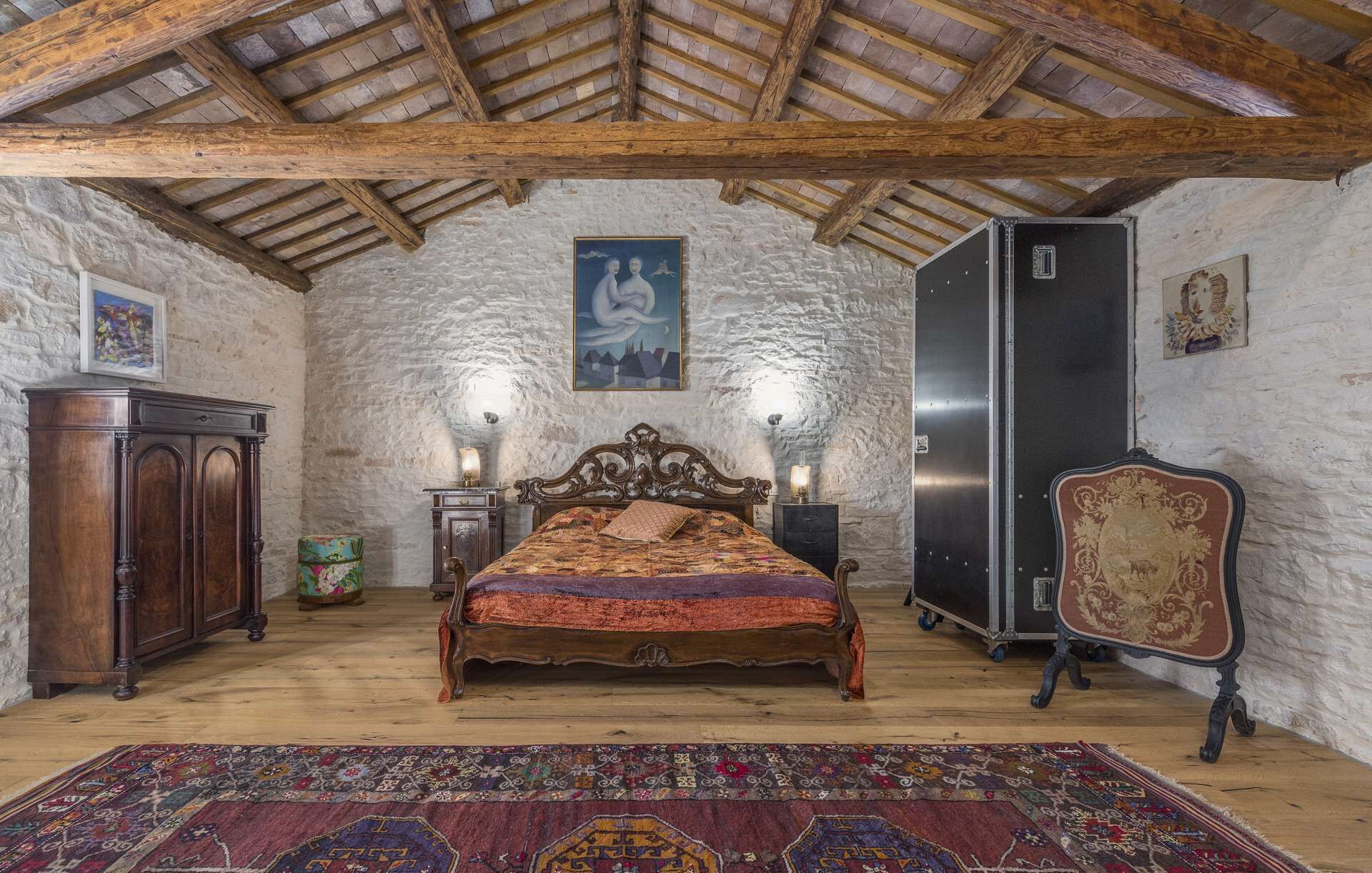A rustic bedroom with a wooden bed, stone walls, a wooden ceiling, and a large rug.