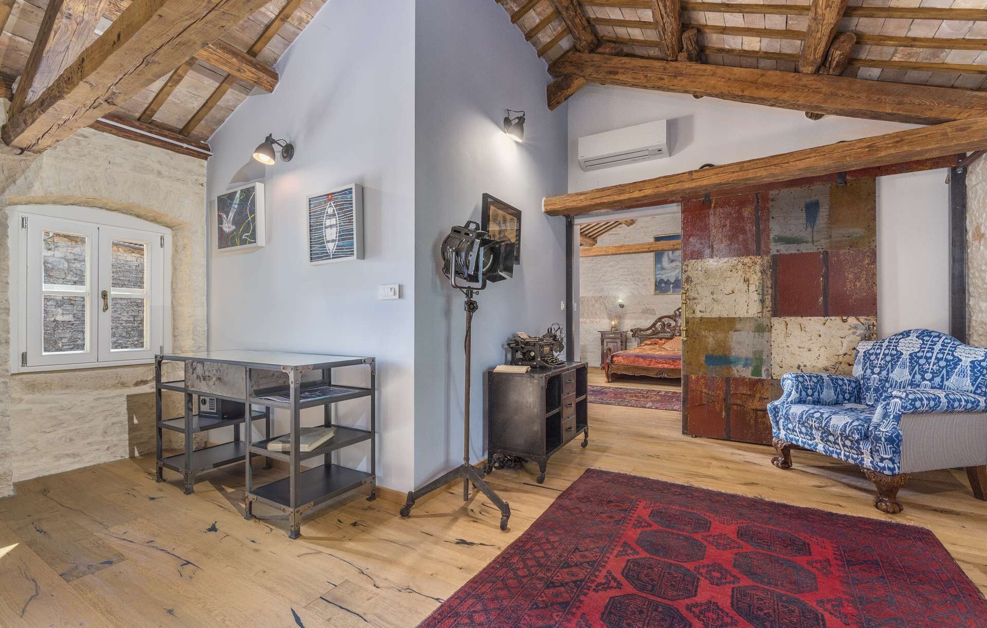 A rustic room with exposed wooden beams, a stone wall, and a traditional sofa.