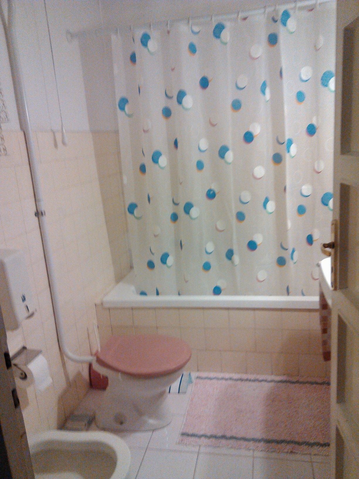 Une salle de bain avec des toilettes, un rideau de douche à pois bleus et blancs, et un tapis de bain rose.