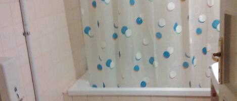 Une salle de bain avec des toilettes, un rideau de douche à pois bleus et blancs, et un tapis de bain rose.