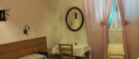 A bedroom with a bed, a desk, a chair, a mirror, and curtains.
