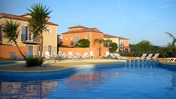 A swimming pool with lounge chairs and palm trees, surrounded by buildings with a Mediterranean architectural style. - Quiet house in the garrigue, 20 minutes from the beach (6 people) (Béziers)