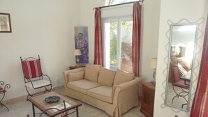 A living room with a beige sofa, a small table, a chair, and a mirror on the wall. - Quiet house in the garrigue, 20 minutes from the beach (6 people) (Béziers)