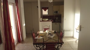 A dining area with a table set for four, a ceiling fan, and a view into the kitchen. - Quiet house in the garrigue, 20 minutes from the beach (6 people) (Béziers)