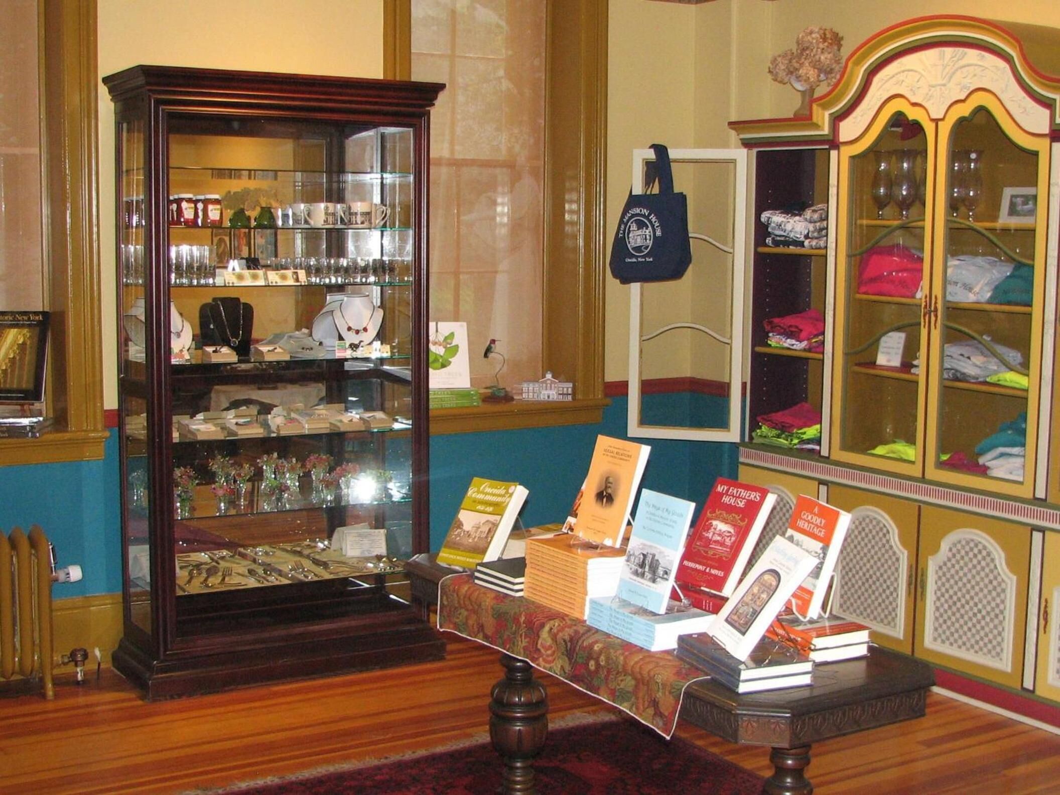 A room with a display case containing various items, a table with books, and a cabinet with folded clothes.