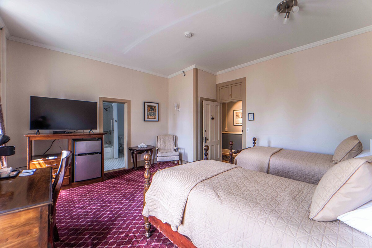 A hotel room with a large bed, a desk with a television, a small refrigerator, and a chair.