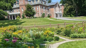 A historic building with a brick facade, a central tower, and a well-maintained garden with a variety of flowers and a gravel path. - Oneida Community Mansion House (Oneida)
