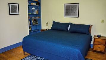 A bedroom with a large bed, a bookshelf, a nightstand, and two framed pictures on the wall.