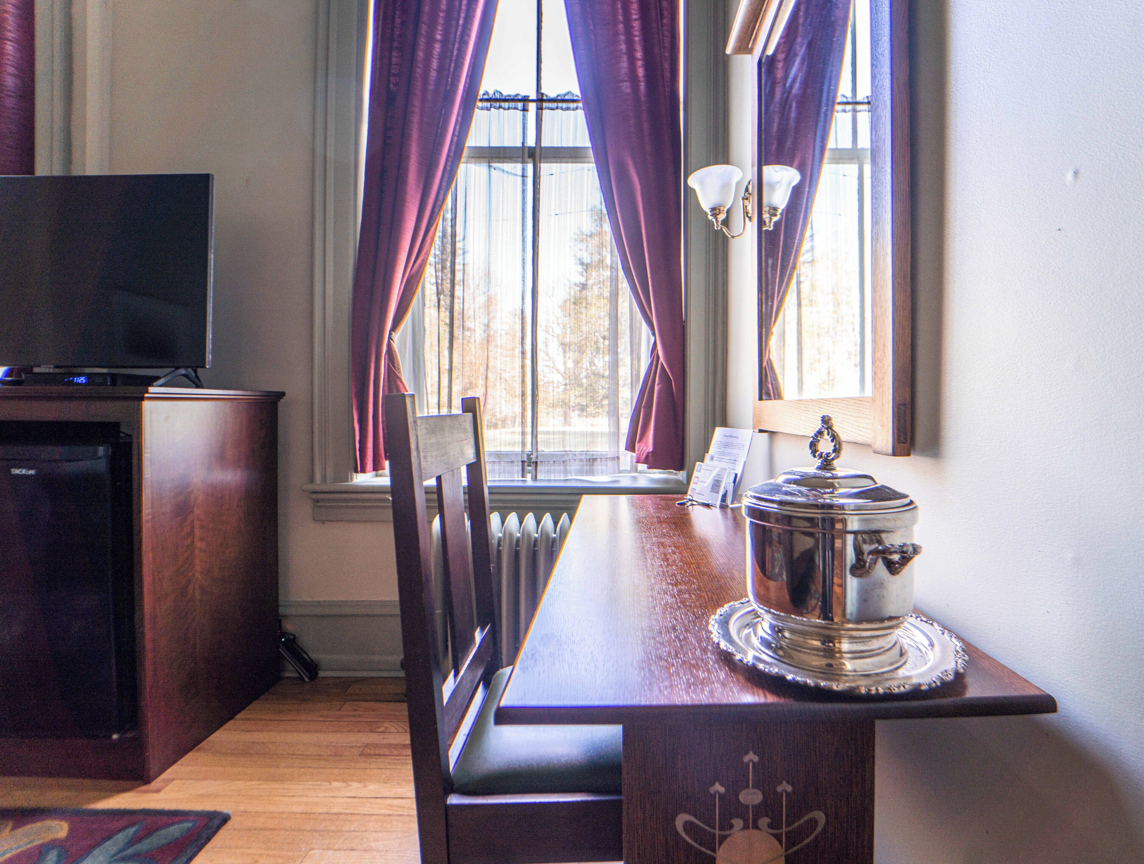 A room with a wooden table, a chair, a television, a window with curtains, and a radiator.
