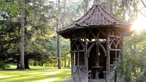 A wooden gazebo with a tiled roof, surrounded by trees and grass in a park. - Oneida Community Mansion House (Oneida)