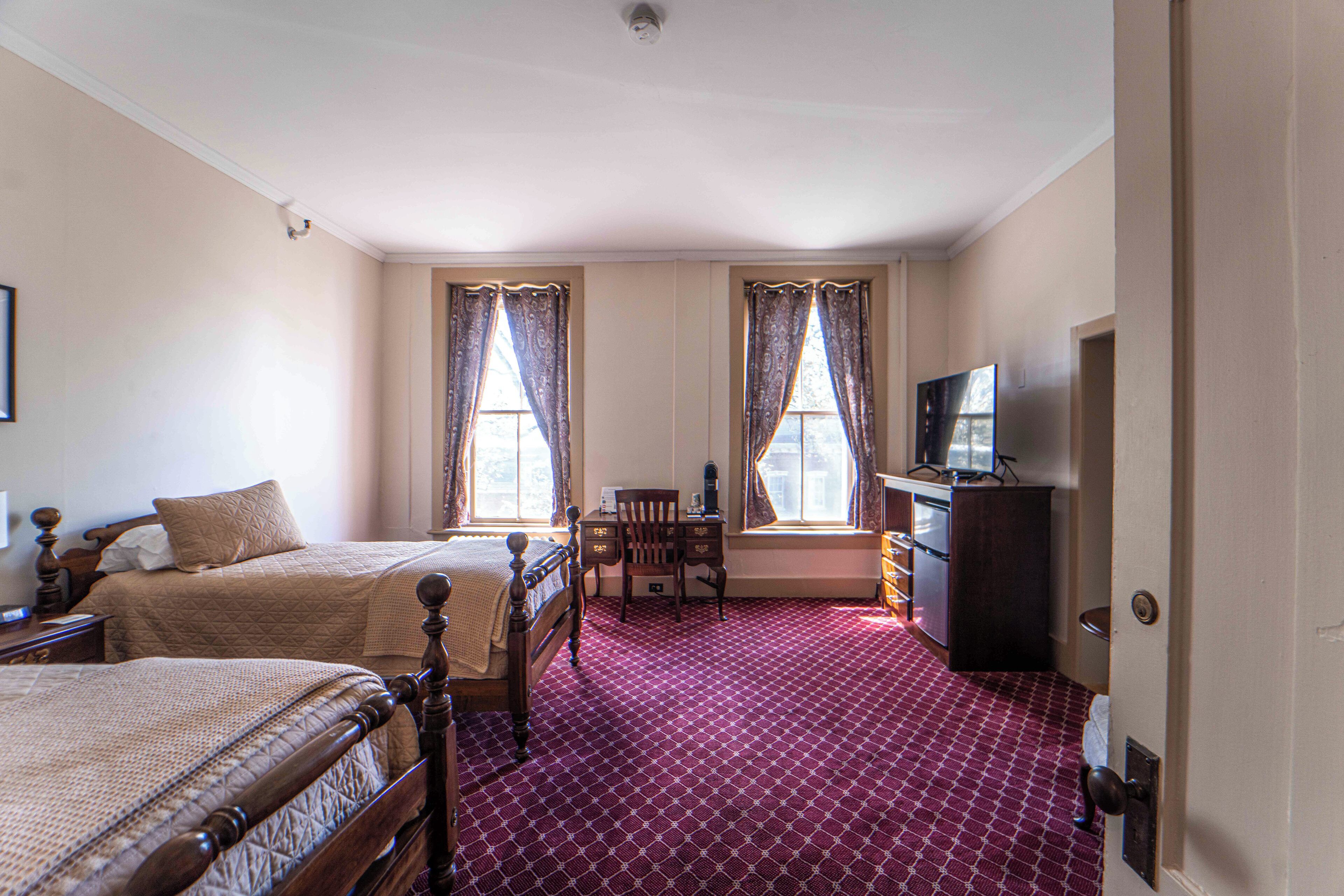 A hotel room with two beds, a desk, a chair, a television, and a wardrobe.