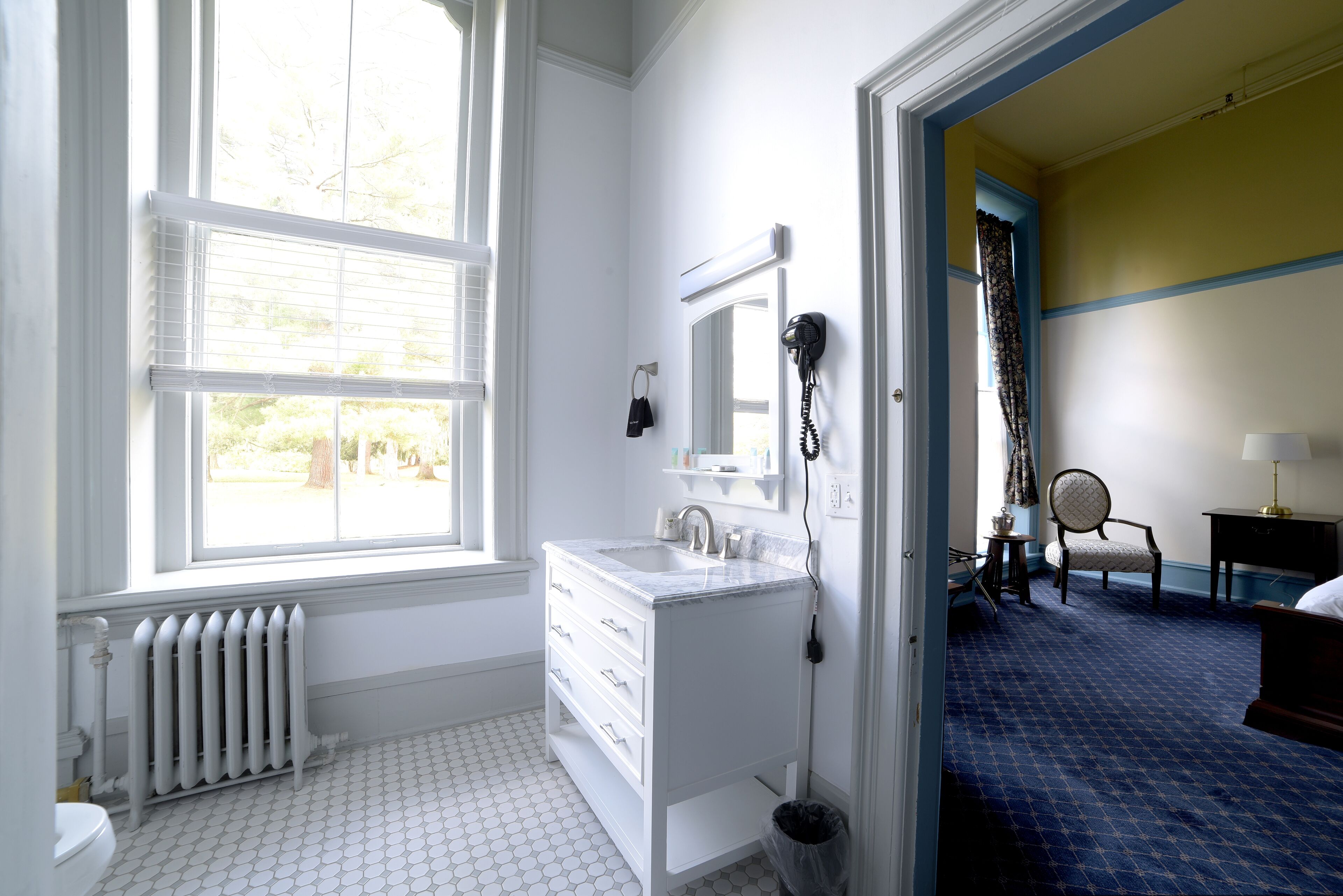 Ein Badezimmer mit weißem Waschtisch, Heizkörper und einem Fenster mit Jalousien.