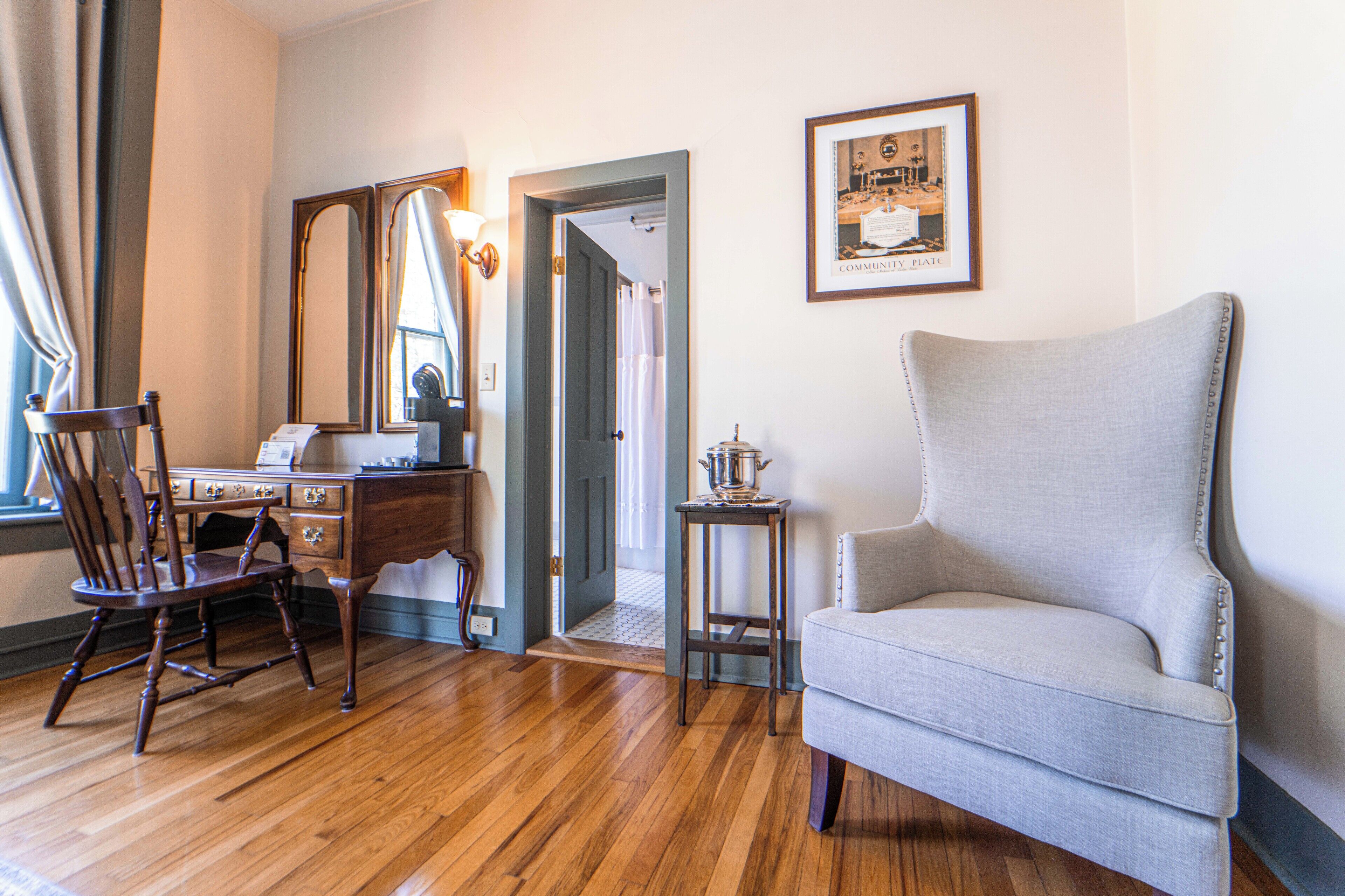 A room with a wooden desk, a chair, a grey armchair, and a framed picture on the wall.